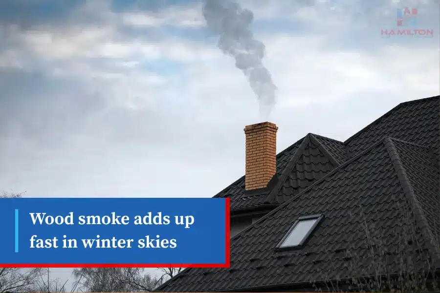 Chimney releasing smoke into winter sky above dark rooftop.